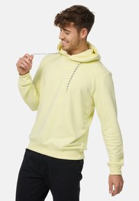 Sudadera ligera amarilla con cordones y un pequeño logo cuadrado, hecha de material suave, con corte holgado y puños acanalados.