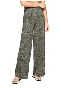 Femme portant un pantalon large taille haute avec un motif abstrait noir, blanc et beige, associé à des sandales ouvertes beige.