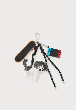 Sleutelhanger met een klein zwart-wit hondenfiguurtje, een miniatuur skatebord, een veter en een klein handheld spelconsole.