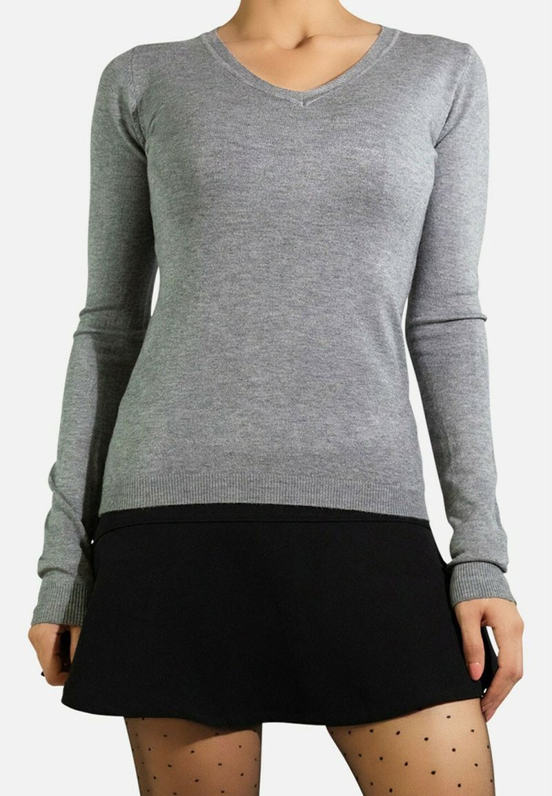 Pull à col en V gris à manches longues, avec des poignets côtelés, assorti à une jupe noire évasée et des collants transparents à pois. Texture lisse, design ajusté.