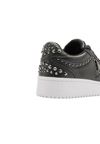 Sneaker in pelle nera con suola in gomma bianca, dotata di borchie argentate sul tallone e sui lati, texture liscia e bordi arrotondati.