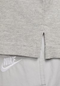 Szürke szövet, textúrált kötött mintával, oldalhasítékkal az alján. Az alsó részen egy fehér Nike logó látható.