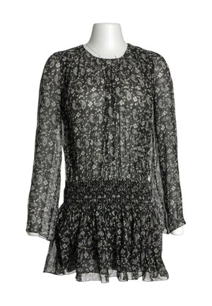 Blusa negra transparente de manga larga con estampados blancos de paisley y flores, cintura fruncida y bajo con volantes sobre un torso de maniquí blanco.