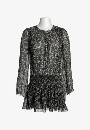 Blusa negra transparente de manga larga con estampados blancos de paisley y flores, cintura fruncida y bajo con volantes sobre un torso de maniquí blanco.