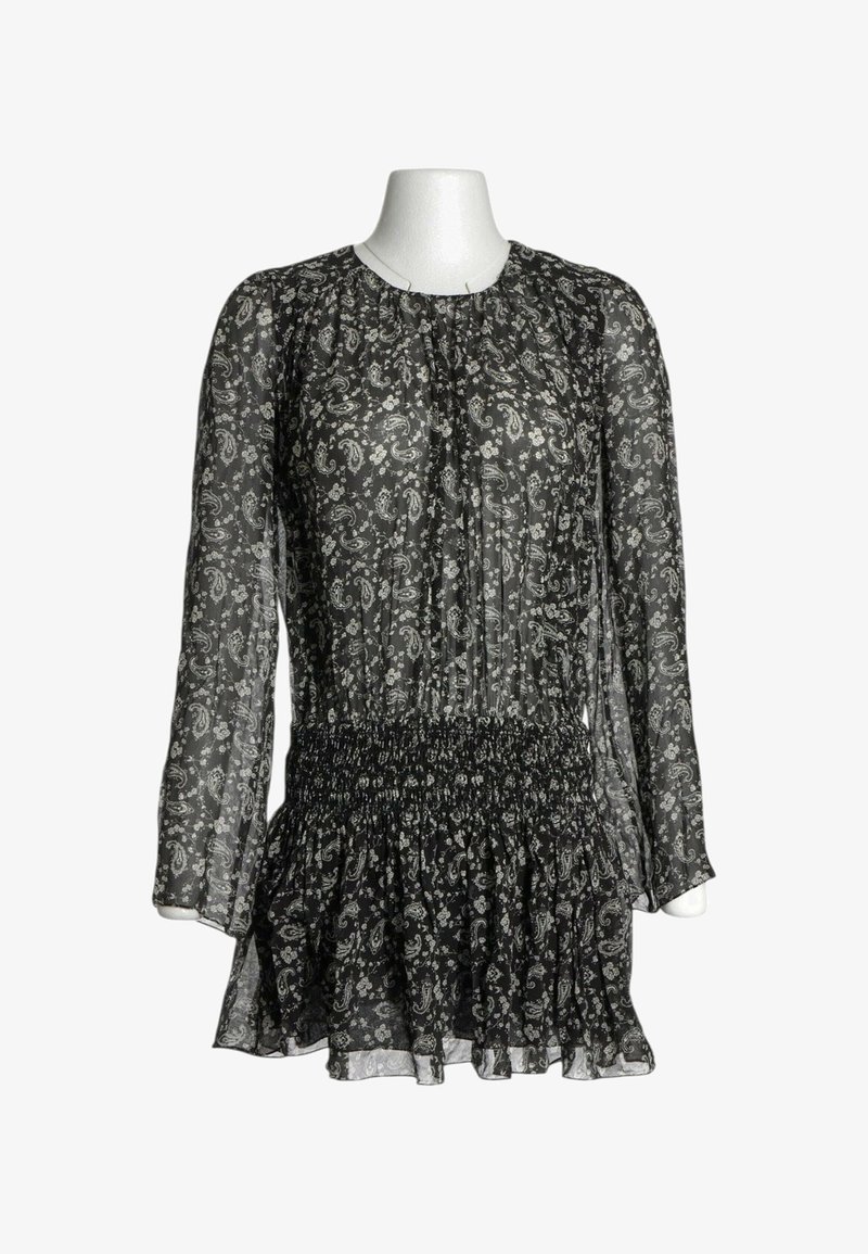 Blouse noire transparente à manches longues avec motifs cachemire et floraux blancs, taille smockée et ourlet volanté sur un buste de mannequin blanc.