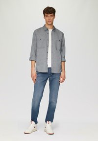 Lichtblauw overhemd met knopen en twee borstzakken, gecombineerd met vervaagde blauwe jeans en witte sneakers met rode accenten. Gladde, casual stoffen.
