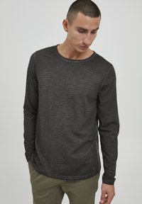 Langærmet sort skjorte med rund hals, lavet af struktureret stof. Har et subtilt meleret mønster og synlige syninger.