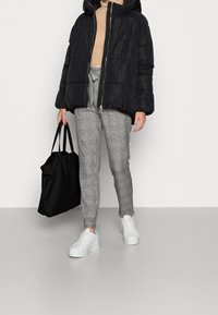 Svart puffjacka med huva, beige polotröja, grå rutiga byxor, vita plattformssneakers och en svart tote-väska.