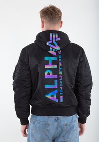 Black bomber jacket with a shiny, iridescent "ALPHA INDUSTRIES" logo on the back. Features a hood and ribbed cuffs and hem.