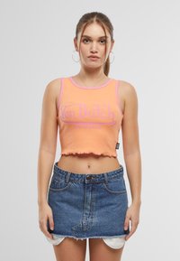 Light orange crop top with pink trim and a fuzzy hem, featuring "Von Dutch ORIGINALS" printed in pink. Paired with a blue denim skirt.