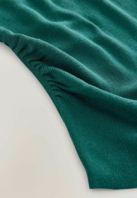 Țesătură tricotată verde, cu o textură moale, având detalii plisate de-a lungul marginii și un țesut uniform, neted.