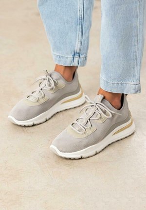 Zapatillas deportivas de color gris claro con parte superior de malla, acentos texturizados, detalles en beige, cordones elásticos y suela de goma blanca con una franja dorada.