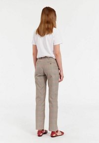 Un pantalon à carreaux brun clair avec une coupe ajustée, un devant plat et des détails en boutons, associé à un t-shirt blanc uni et des sandales plates rouges.