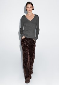 Szary sweter z długim rękawem i dekoltem w serek, w połączeniu z fakturowanymi brązowymi spodniami z weluru. Strój charakteryzuje się luźnym krojem i kieszeniami w spodniach.