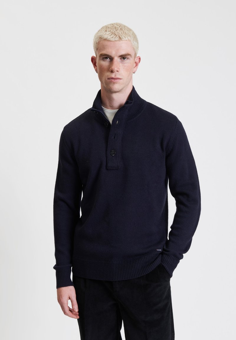 Maglione girocollo lavorato a maglia di colore navy con colletto alto, pattina con due bottoni, polsini e orlo ribattuti e un motivo a trama sul colletto.