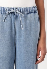 Lyseblå denim joggebukser med elastisk linning og snor, med en avslappet passform og subtil tekstur.