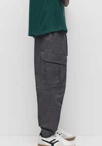 Grå cargo bukser med flere lommer, tapered ben design, lavet af bomuldsstof. Parret med en grøn t-shirt og hvide sneakers.