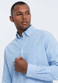 Camisa de botones azul claro en una tela suave, con un bolsillo en el pecho, mangas largas y puños abotonados, con un diseño de cuello clásico.