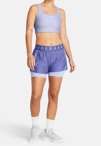 Set di reggiseno sportivo e pantaloni corti viola caratterizzato da un tessuto morbido, una vita elastica con il testo "UNDERARMOUR" e un design leggero e traspirante.