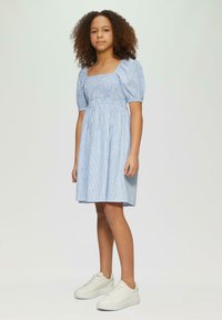 Blau gestreiftes Kleid mit Puffärmeln, quadratischem Ausschnitt und elastischem Oberteil. Kombiniert mit weißen Sneakers. Glattes Material, knielang.
