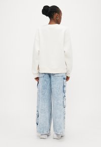 Εκρού φαρδιά φούτερ με ριμπ μανσέτες, συνδυασμένο με ανοιχτόχρωμα καμπάνια cargo τζιν με πλαϊνές τσέπες και άνετη εφαρμογή.