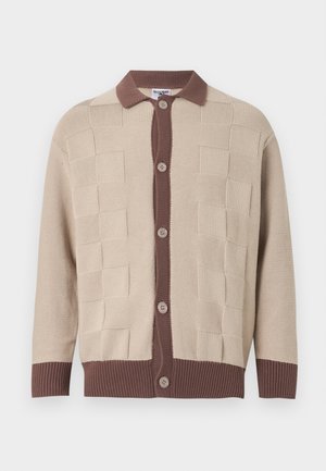 Μπεζ πλεκτή ζακέτα με υφασμάτινα τετράγωνα σχέδια, καφέ πατζάκι κουμπιών, γιακά, μανσέτες και ζώνη μέσης, με πέντε μπεζ κουμπιά μπροστά.