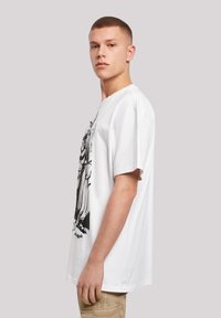 Hvit bomulls t-skjorte med kort erme og oversized passform, med et svart grafisk trykk på forsiden. Enfarget bakside og sidevisning vist.