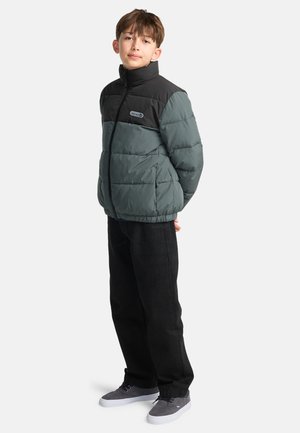 Doudoune gris foncé avec un panneau supérieur noir, fermeture éclair à l'avant et col haut. Associée à un jean noir et des sneakers gris.