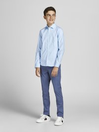Chemise bleu clair, coupe ajustée, manches longues. Associée à un pantalon bleu et des chaussures blanches avec des accents rouge foncé et marine.