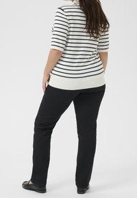 Kremowa bluzka z krótkim rękawem w paski niebieskie, zestawiona z czarnymi spodniami i płaskimi butami. Bluzka ma prążkowany dół i dopasowany krój.