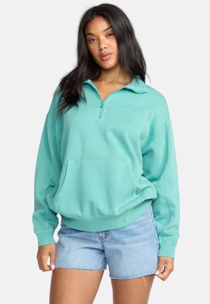 Teal kwart rits pullover sweatshirt met een voorzak, een relaxte fit en geribbelde manchetten. Gecombineerd met lichtblauwe denim shorts.