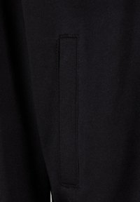 Sorte stof med en glat tekstur og en syet lomme detalje på siden, der subtilt integreres i det overordnede design.