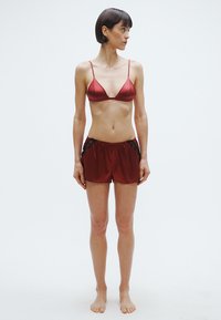 Bralet roșu din satin cu bretele subțiri, asortat cu pantaloni scurți cu accente de dantelă neagră, textură netedă și croială lejeră.