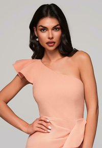 Asymmetrisk kjole med én skulder i myk ferskenfarget stoff med volangdetalj, som har et tettsittende liv og elegant Drapering i midjen.