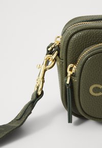 Groene gestructureerde leren tas met gouden hardware, voorzien van een afneembare schouderband en ritssluiting. Opvallend logo aan de voorkant.