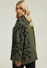 Zielona oliwkowa, oversize'owa sweter z czarnym wzorem w panterę, ze ściągaczami na rękawach i u dołu. Miękka faktura i luźny krój.