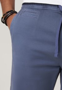 Jasnoniebieskie spodnie dresowe wykonane z gładkiego materiału, z elastycznym pasem i sznurkiem do regulacji oraz tylną kieszenią po prawej stronie.