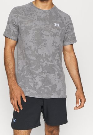 Mand iført grå camouflage-mønstret Under Armour t-shirt og sorte Under Armour shorts, stående mod en ensfarvet baggrund.
