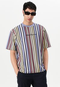 Striped cotton t-shirt featuring vertical lines in blue, yellow, red, and black. Crew neck, loose fit, with embroidered text on the front.