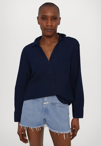 Marinblå skjorta med knappar, krage, långa ärmar och avslappnad passform, i kombination med ljusblå denimshorts med fransade kanter.