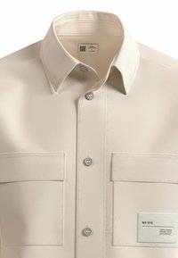 Beige, korteblauw overhemd met een button-down kraag, twee voorkruiszakken, zichtbare stiksels en een stoffen label met de tekst "GEEN VERF."