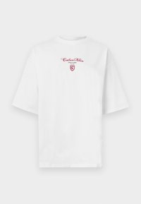 Fehér, túlméretezett rövid ujjú póló piros "Calvin Klein New York EST 1968" felirattal és egy kis pajzs logóval a mellkason.