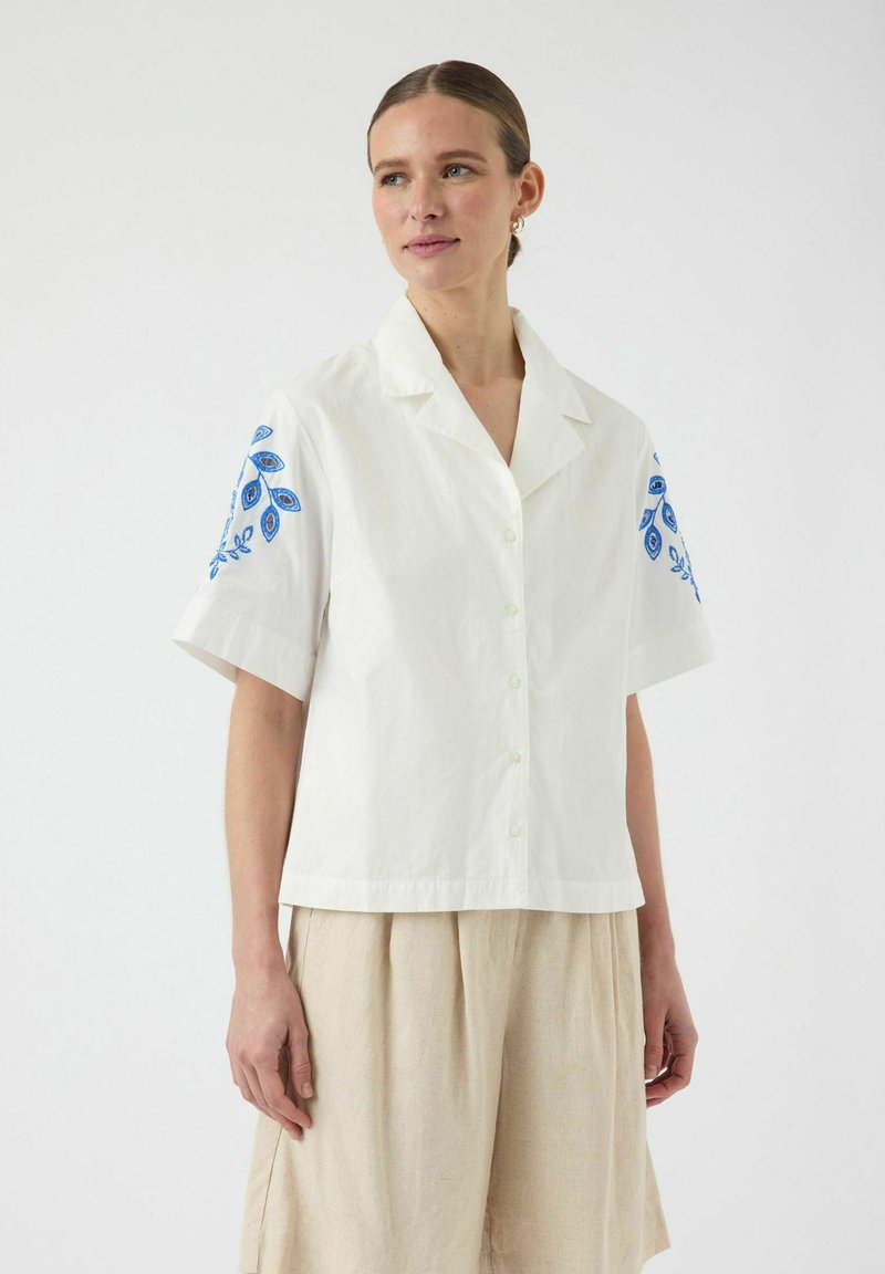 Hvit kortermet skjorte med blå brodert blomstermønster på skuldrene, med knappefront og avslappet passform.