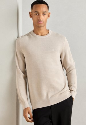 Light beige long-sleeve sweater with a round neck and ribbed cuffs, featuring a textured knit pattern and a subtle logo on the chest.
