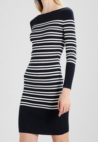 Abito a maglia a righe blu navy e bianche con scollo tondo, maniche lunghe e silhouette aderente, caratterizzato da una texture a costine e orlo sopra il ginocchio.