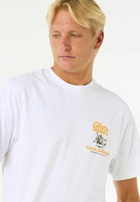 Hvid bomulds T-shirt med rund halsudskæring og korte ærmer, der har en farverig grafisk print på venstre bryst, inklusive tekst og illustrationer.