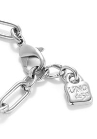 Bracelet en chaîne de métal argenté avec de gros maillons, un fermoir mousqueton et un pendentif cadenas gravé "UNO de 50". Texture lisse.