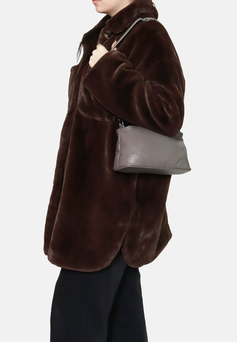 Cappotto di pelliccia sintetica marrone con colletto alto e tasche laterali, indossato con una borsa a spalla in pelle grigia dal texture liscia e design semplice.