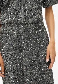 Vestido de lentejuelas en gris con una superficie texturizada adornada con lentejuelas circulares brillantes, mangas cortas y un corte relajado.