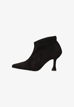 Botín de ante negro con punta puntiaguda, tacón stiletto delgado y diseño sin costuras, que presenta una textura suave y una silueta elegante.